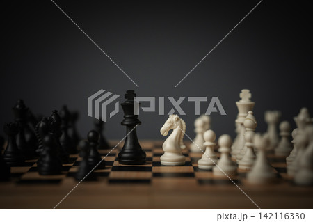 full chess set mid-game on wooden board, dark moody lighting full chess set mid-game on wooden board, dark moody lighting 142116330