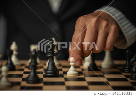 hand placing a white chess pawn on wooden board hand placing a white chess pawn on wooden board 142116335