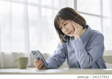 スマートフォンを見ながら考え込む50代前半の女性 142117912