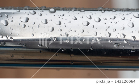 Close up view of a stainless steel handrail. Covered in fresh morning raindrops and water droplets. 142120064