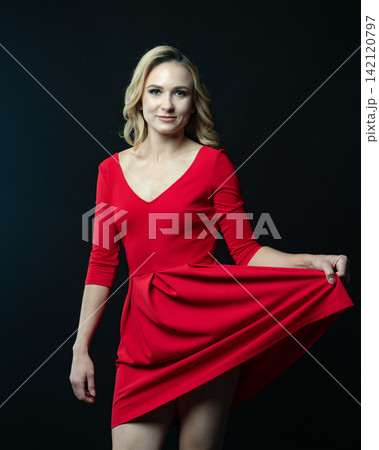 Elegant blonde woman posing in red dress on black background Elegant blonde woman posing in red dress on black background 142120797