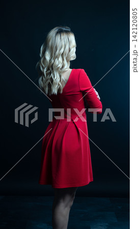Elegant blonde woman posing in red dress on black background Elegant blonde woman posing in red dress on black background 142120805