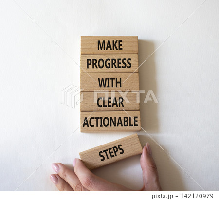 Make progress with clear actionable steps symbol. Concept words make progress with clear actionable steps on wooden blocks. Businessman hand. Beautiful white background. Business concept. Copy space. Make progress with clear actionable steps symbol. Concept words make progress with clear actionable steps on wooden blocks. Businessman hand. Beautiful white background. Business concept. Copy space. 142120979