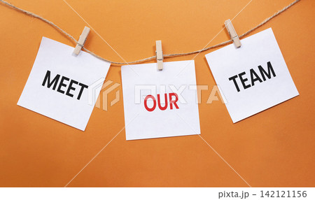 Meet Our Team text on white paper notes hanging on rope with clothespins over orange background. Team introduction and corporate culture concept with copy space. Meet Our Team text on white paper notes hanging on rope with clothespins over orange background. Team introduction and corporate culture concept with copy space. 142121156