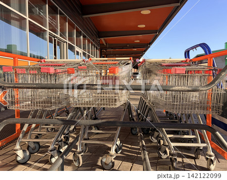 Row of empty metal shopping carts with red handles parked outside a modern supermarket Row of empty metal shopping carts with red handles parked outside a modern supermarket 142122099