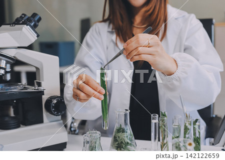 Scientists in lab coats work with plants in a modern lab, focusing on research and experimentation under bright, sterile conditions. Scientists in lab coats work with plants in a modern lab, focusing on research and experimentation under bright, sterile conditions. 142122659