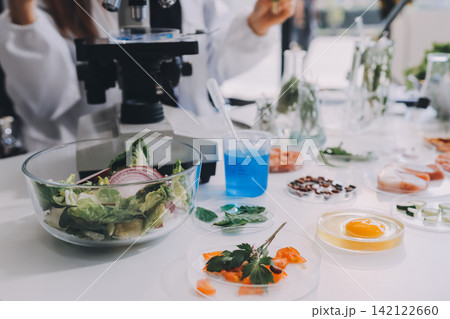 Scientists in lab coats work with plants in a modern lab, focusing on research and experimentation under bright, sterile conditions. 142122660