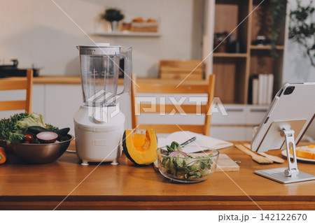 Woman preparing green smoothie in bright kitchen with fresh fruits and vegetables, healthy eating lifestyle moment in natural daylight 142122670
