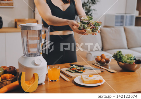 Woman preparing green smoothie in bright kitchen with fresh fruits and vegetables, healthy eating lifestyle moment in natural daylight Woman preparing green smoothie in bright kitchen with fresh fruits and vegetables, healthy eating lifestyle moment in natural daylight 142122674