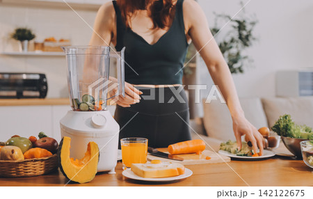 Woman preparing green smoothie in bright kitchen with fresh fruits and vegetables, healthy eating lifestyle moment in natural daylight 142122675