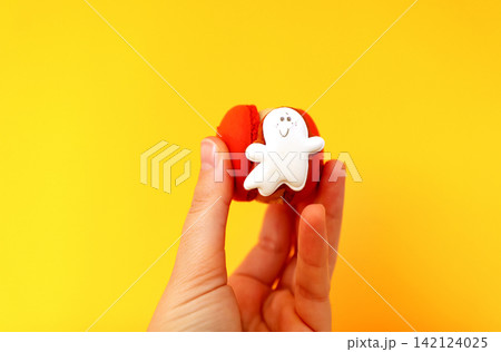 Hand holding a Halloween red macaron cookie decorated with a cute little white ghost figure on a bright yellow background. a cute Halloween ghost macaron cookie Hand holding a Halloween red macaron cookie decorated with a cute little white ghost figure on a bright yellow background. a cute Halloween ghost macaron cookie 142124025