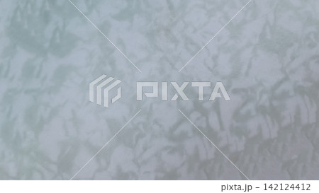 Abstract background of a mottled, textured surface in soft gray and greenish blue tones. Uneven, rippled patterns resemble crumpled paper or cloud like formations under diffused lighting... Abstract background of a mottled, textured surface in soft gray and greenish blue tones. Uneven, rippled patterns resemble crumpled paper or cloud like formations under diffused lighting... 142124412