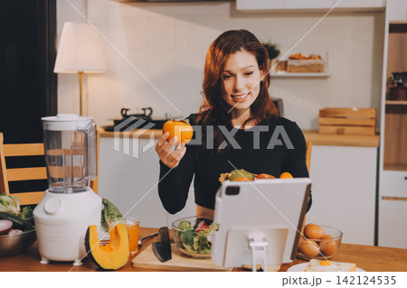 Woman preparing green smoothie in bright kitchen with fresh fruits and vegetables, healthy eating lifestyle moment in natural daylight 142124535