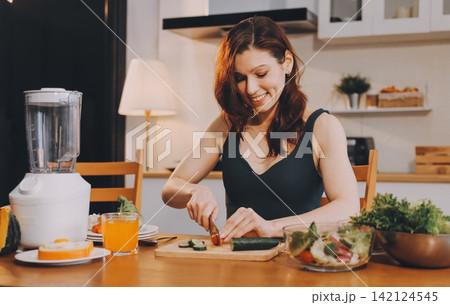 Woman preparing green smoothie in bright kitchen with fresh fruits and vegetables, healthy eating lifestyle moment in natural daylight Woman preparing green smoothie in bright kitchen with fresh fruits and vegetables, healthy eating lifestyle moment in natural daylight 142124545