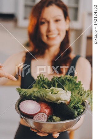 Woman preparing green smoothie in bright kitchen with fresh fruits and vegetables, healthy eating lifestyle moment in natural daylight 142124552