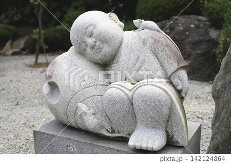 お寺の境内に設置された木魚を枕に居眠りする少年修行僧の石仏 お寺の境内に設置された木魚を枕に居眠りする少年修行僧の石仏 142124864