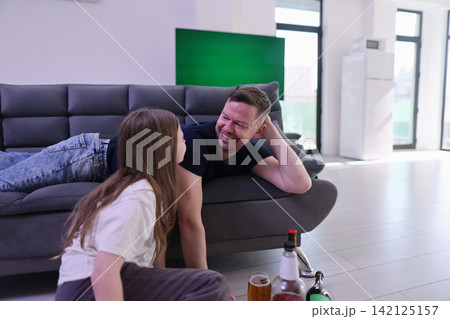 man and woman relaxing together in a modern living room with casual and relaxed atmosphere, eye-level perspective, fabric couch, wooden coffee table, glass beer bottles. man and woman relaxing together in a modern living room with casual and relaxed atmosphere, eye-level perspective, fabric couch, wooden coffee table, glass beer bottles. 142125157