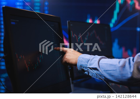 Business person pointing at stock market charts on computer monitors in a dark trading office Business person pointing at stock market charts on computer monitors in a dark trading office 142128644
