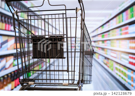 Empty shopping cart in a supermarket aisle with stocked shelves and soft blurred background 142128679