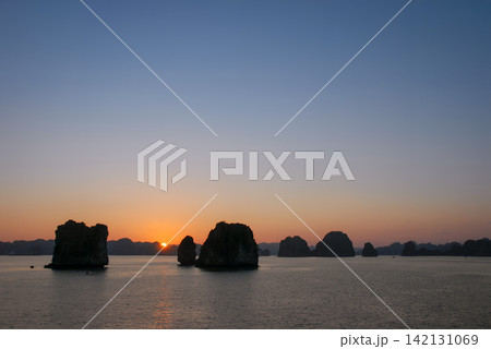 The sun setting over Halong Bay in Vietnam where small islands rise from the water. Sunset view with sun touching the horizon. 142131069