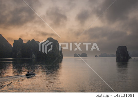 Halong Bay in Vietnam in the early morning before sunrise. The clouds reflect in the water. Dawn view of Halong Bay with pink sky and a small boat. 142131081