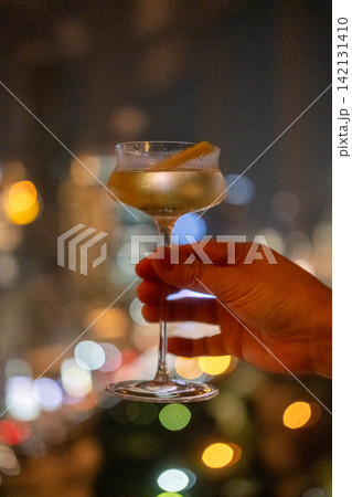A hand holding a glass of cocktail with colorful night city view on the background A hand holding a glass of cocktail with colorful night city view on the background 142131410