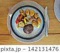 Roasted baby potatoes with beef patty and grilled vegetables served on ceramic plate over wooden table, simple homemade meal viewed from above 142131476