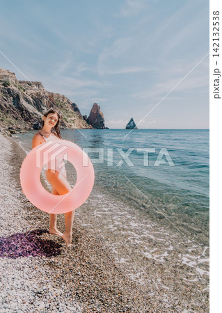 Girl beach inflatable ring stands on a pebble shore with a pink floaty enjoying summer vacation by the sea Girl beach inflatable ring stands on a pebble shore with a pink floaty enjoying summer vacation by the sea 142132538
