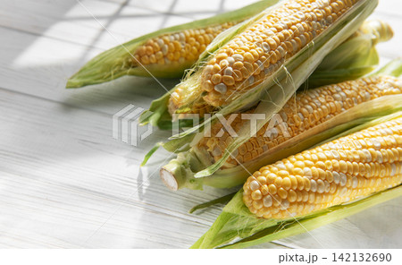 Fresh corn cobs with green husks on white wooden table 142132690