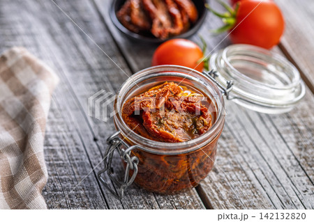 Jar of Sun-Dried Tomatoes in Olive Oil on Rustic Wooden Table with Fresh Tomatoes 142132820