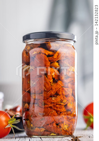 Jar of Sun-Dried Tomatoes in Oil on Rustic Wooden Table With Bowl and Fresh Tomatoes 142132823