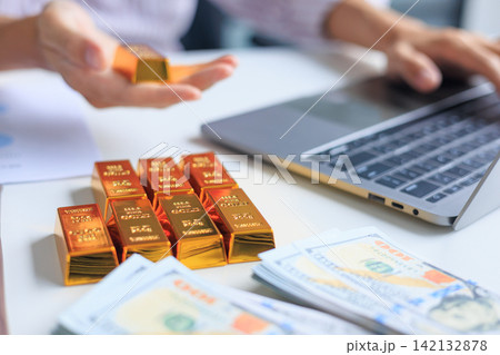 Banker, Accountant or Investor Using Laptop to Manage Online Investment Trading Account with Gold Bars and Cash on the Table. Secure Financial Investment and Wealth Preservation Concept. Banker, Accountant or Investor Using Laptop to Manage Online Investment Trading Account with Gold Bars and Cash on the Table. Secure Financial Investment and Wealth Preservation Concept. 142132878