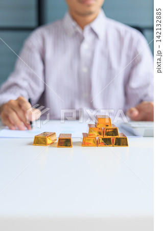 Selective focus on gold bars with background of hands using calculator for gold trading analysis. Concept for wealth management, asset protection, and financial planning. Selective focus on gold bars with background of hands using calculator for gold trading analysis. Concept for wealth management, asset protection, and financial planning. 142132885