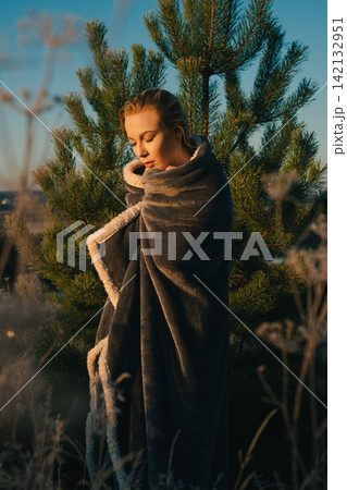 Woman wrapped in cozy blanket among pine trees at golden hour Woman wrapped in cozy blanket among pine trees at golden hour 142132951