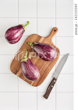 Three fresh purple eggplants  on wooden cutting board 142133397