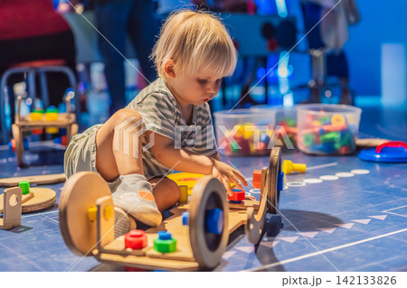 Three year old toddler sitting alone and playing with wooden learning toy at science center, early STEM education, curiosity and child development concept 142133826