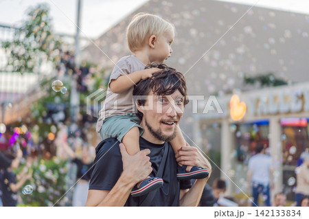 Dad smiles with a three year old child among colorful holiday decorations, showing fatherhood, family celebration and festive outing concept Dad smiles with a three year old child among colorful holiday decorations, showing fatherhood, family celebration and festive outing concept 142133834