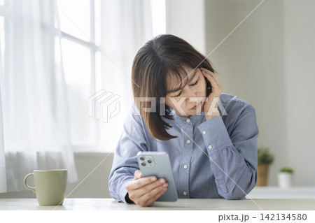スマートフォンを見ながら考え込む50代前半の女性 142134580