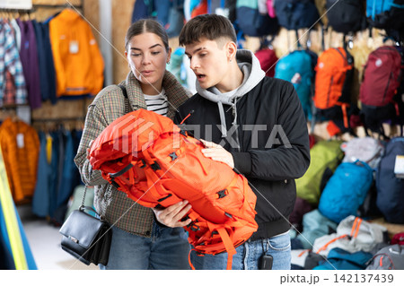 Young married couple in winter clothes chooses a durable backpack for a winter hike in tourist equipment store 142137439