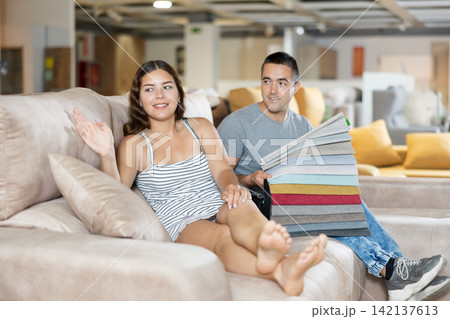Smiling woman and man choosing upholstery for sofa in furnishing store Smiling woman and man choosing upholstery for sofa in furnishing store 142137613