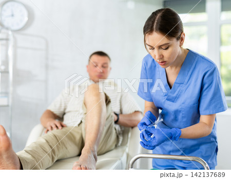 Young woman doctor doing knee injection for the patient lying on clinical chair 142137689