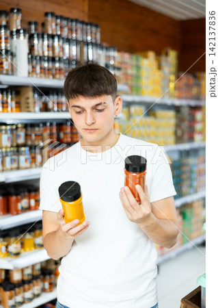 Guy chooses jars of spices in the grocery department of hypermarket Guy chooses jars of spices in the grocery department of hypermarket 142137836
