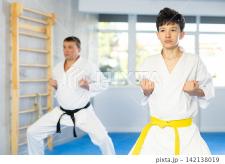 Teen boy wearing kimono training karate techniques during workout session Teen boy wearing kimono training karate techniques during workout session 142138019