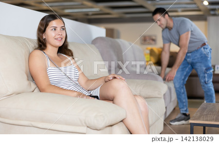 In furniture store,young girl is sitting on sofa with ottoman 142138029