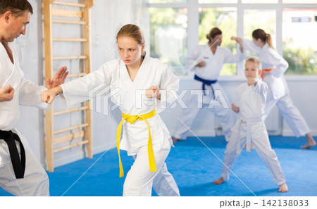 Teen girl at group training in gym practice karate punch block technique with trainer Teen girl at group training in gym practice karate punch block technique with trainer 142138033