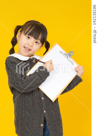 A confident and adorable Asian girl smiles as she holds up a white writing board against a bright yellow background in the studio. A confident and adorable Asian girl smiles as she holds up a white writing board against a bright yellow background in the studio. 142138186