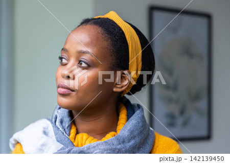 African American woman wearing mustard headband and sweater with gray scarf, gazing left at home African American woman wearing mustard headband and sweater with gray scarf, gazing left at home 142139450