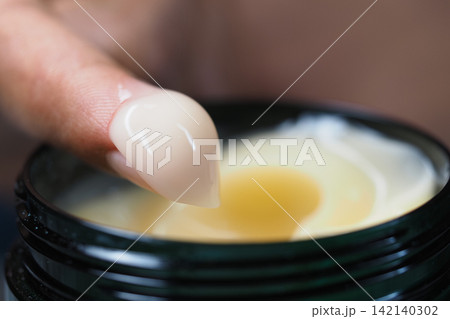 Close look at hand applying cream from container 142140302