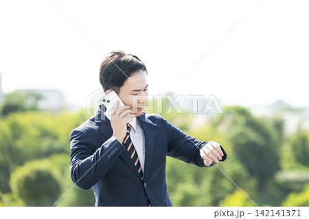 腕時計を見ながら電話をするビジネスマン 142141371
