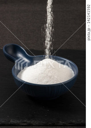 fine White Table Salt Pouring into Blue Bowl 142141592